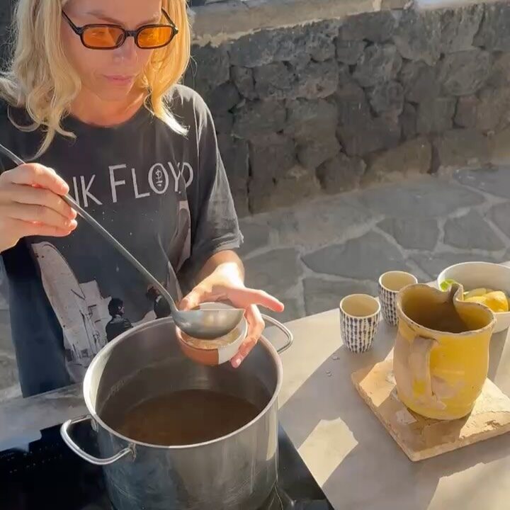 Ladle of dark beef bone broth lifted from a stockpot in warm kitchen light