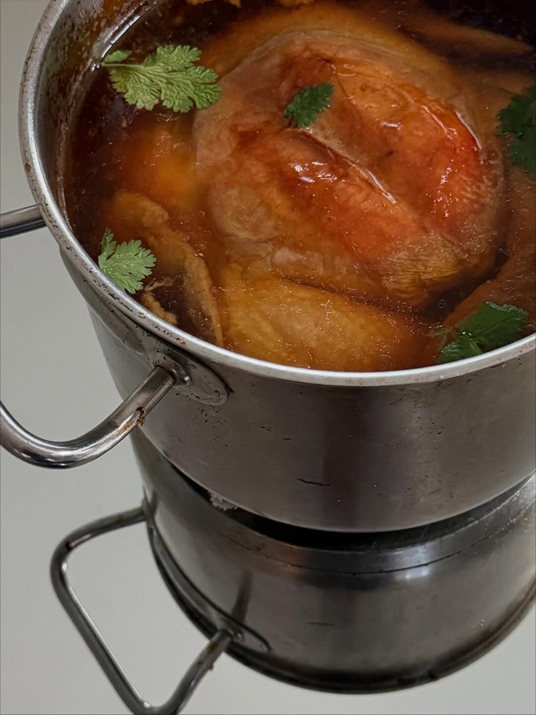 Whole organic chicken simmering with fresh herbs in a stockpot