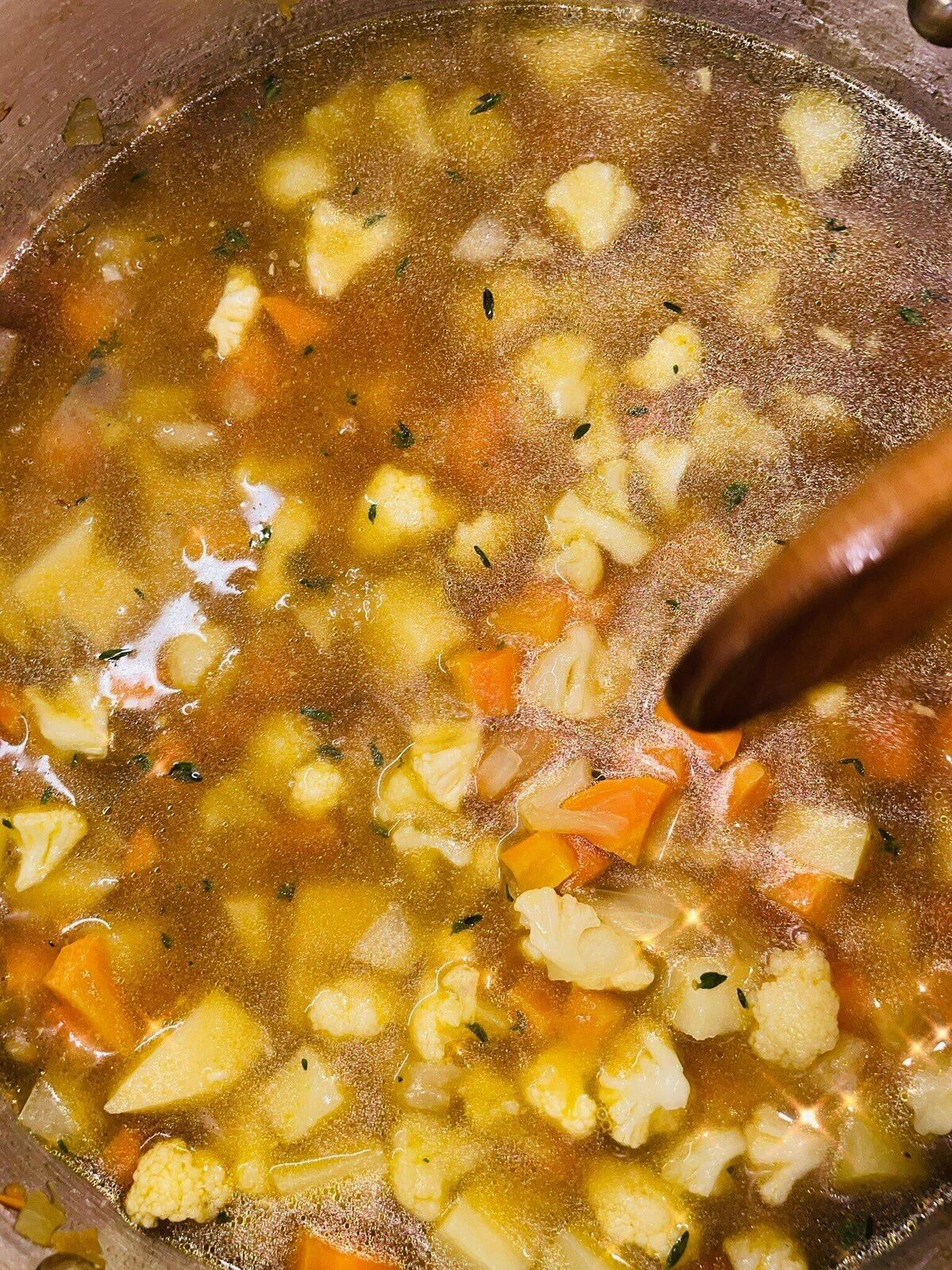 A bowl of creamy chicken and vegetable soup with thyme on top