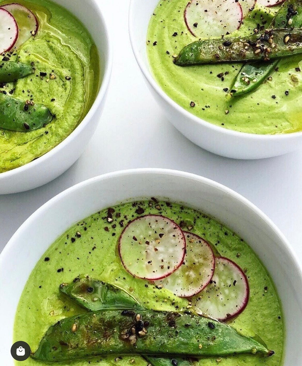 A pale green creamy soup garnished with snap peas and seeds
