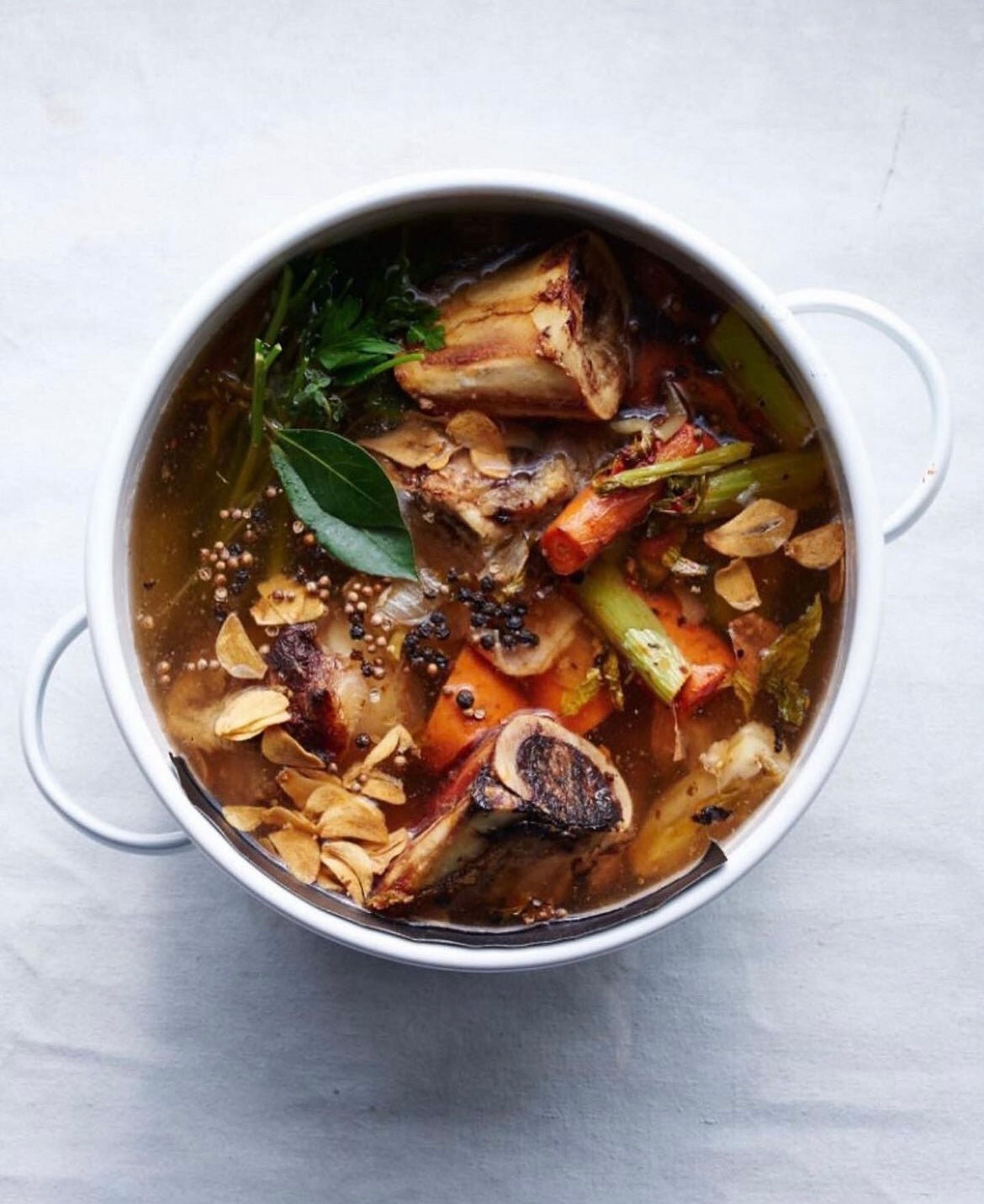 A deep bowl of beef stew with roasted tomatoes and fresh herbs
