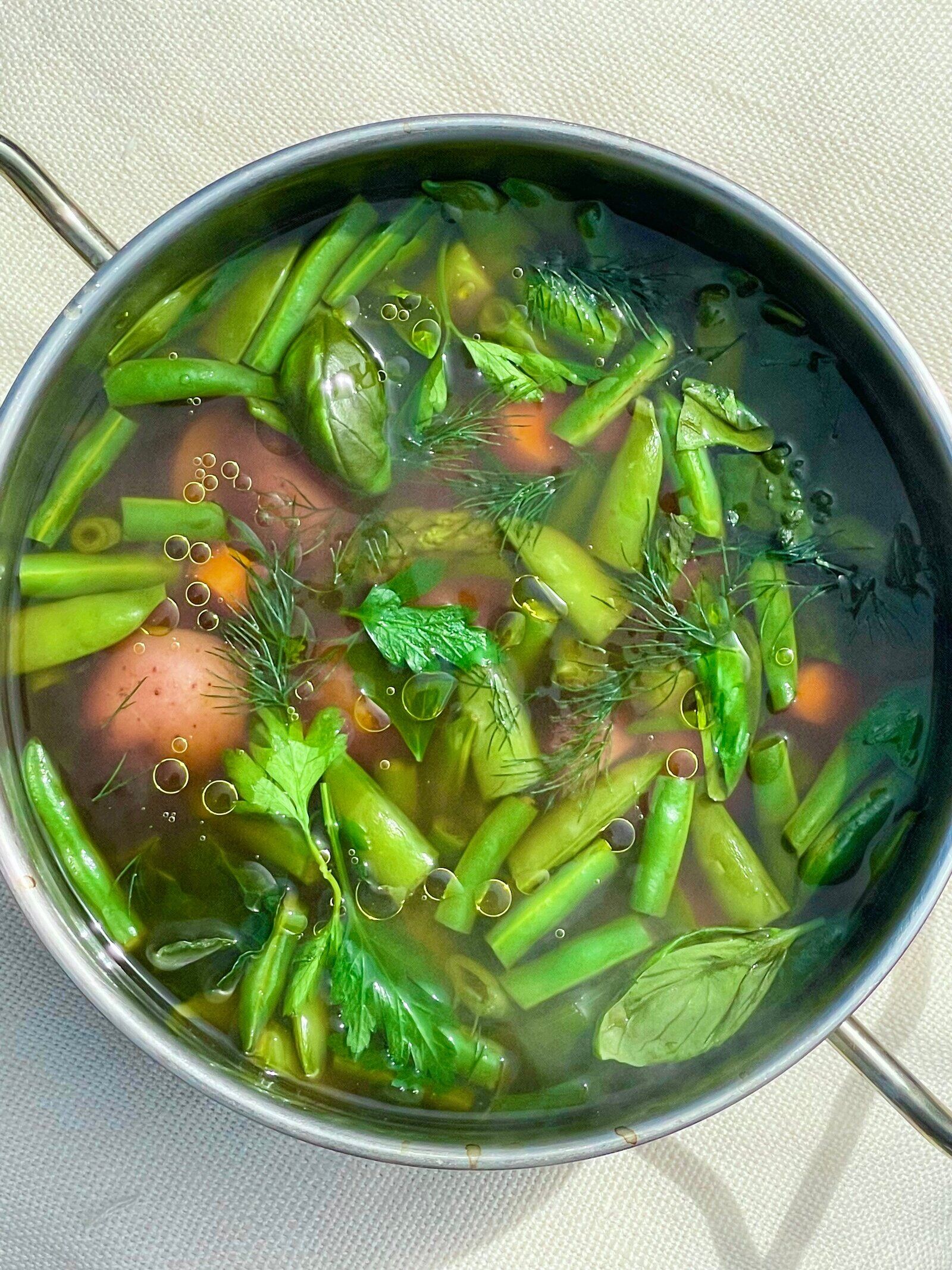 A bowl of clear broth with new potatoes, green beans and herbs