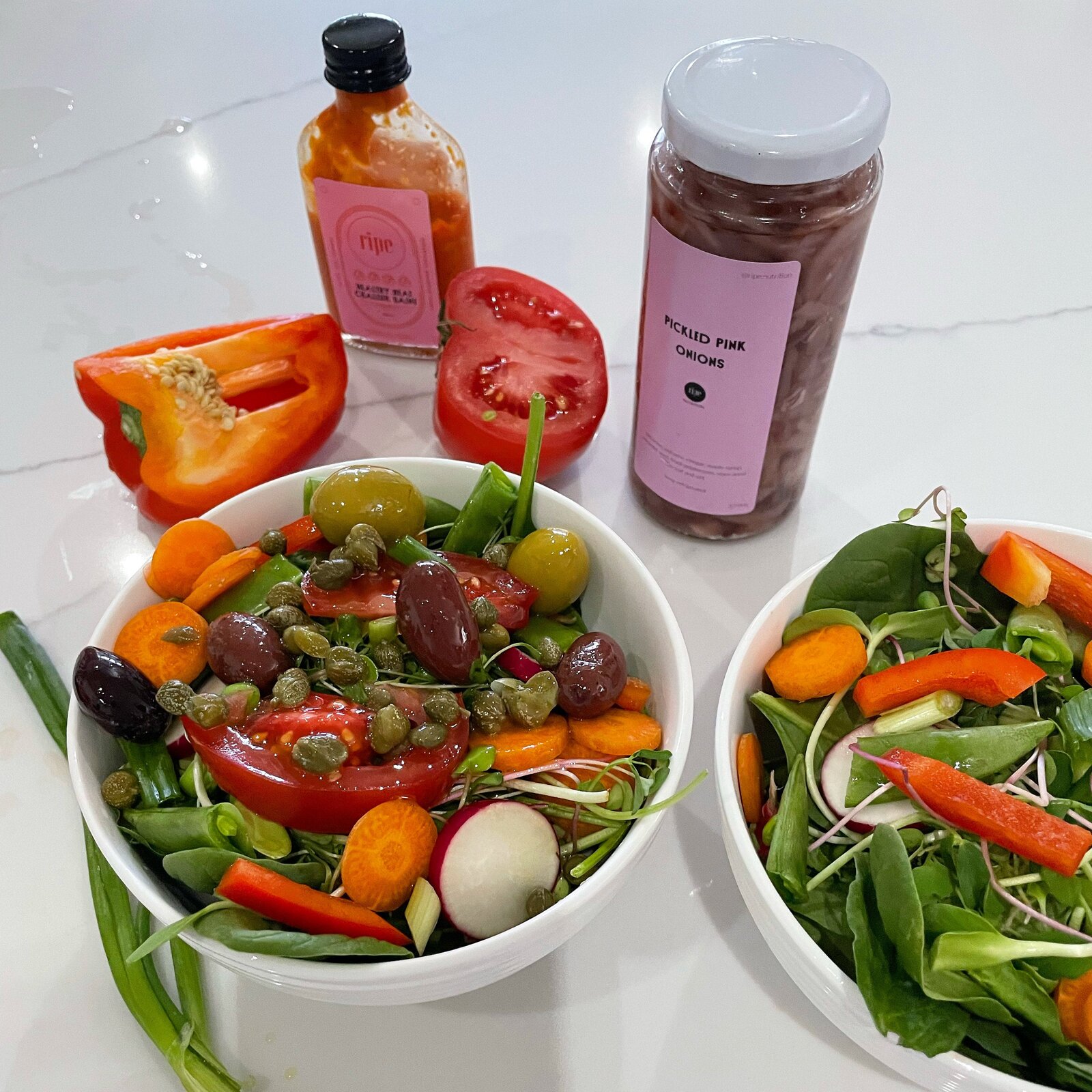 A bowl of salad with leaves, peppers, avocado and olives