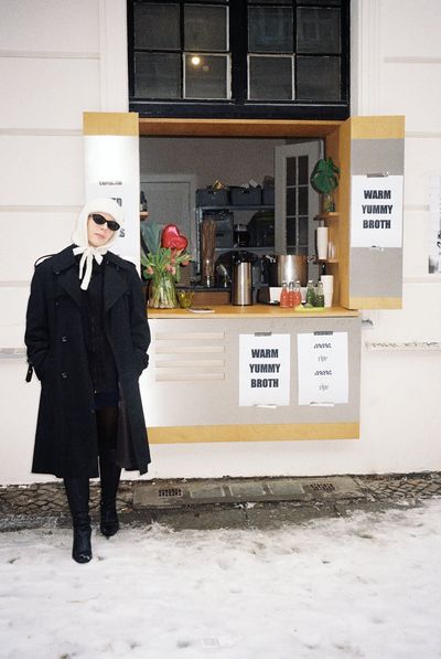 Sinead McInerney standing in front of the RIPE Lifestyle Europe pop-up window in Berlin — snow on the ground, hand-printed 'warm yummy broth' signs in the window