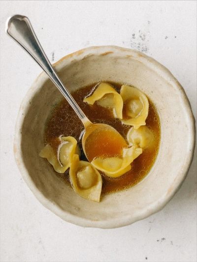 Bone broth with pasta in a rustic stoneware bowl, top-down
